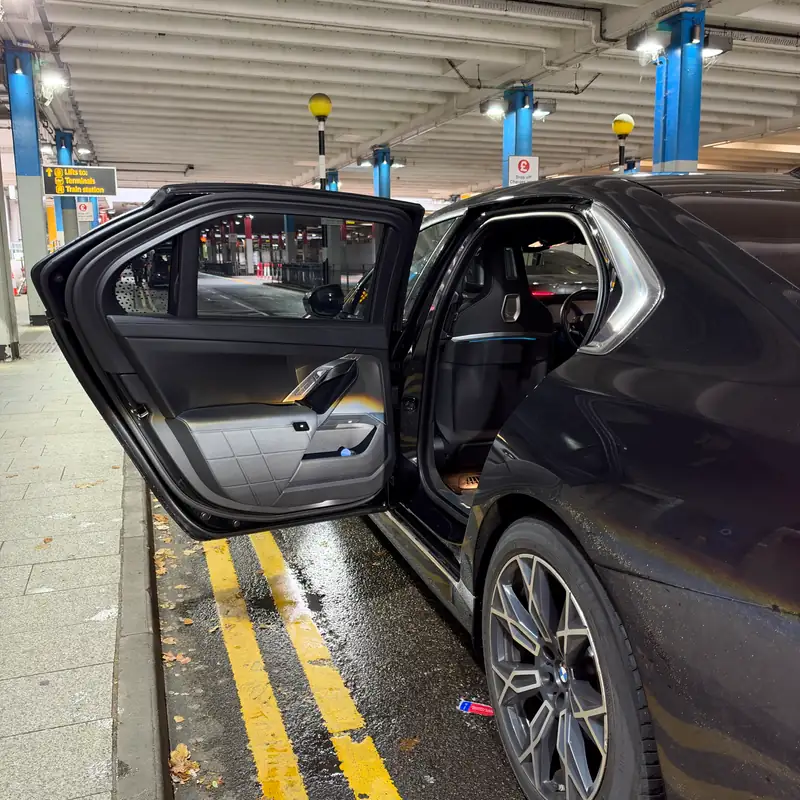 Open door of luxury BMW i7 chauffeur car displaying executive interior at Gatwick airport terminal drop-off